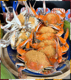 Cooked blue crabs sprinkled with a golden-brown seasoning mix, arranged on a blue plate on a wooden serving tray.