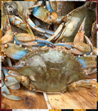 A pile of live blue crabs on a wooden surface, showing their blue and green shells with orange accents. A watermark logo for 'The Crab King' is visible in the top-left corner.